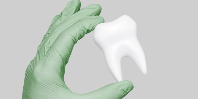 Hand in green glove holding a 3D tooth model.