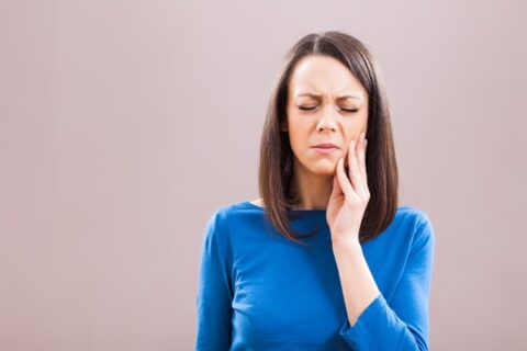 Woman experiencing toothache, holding her cheek.